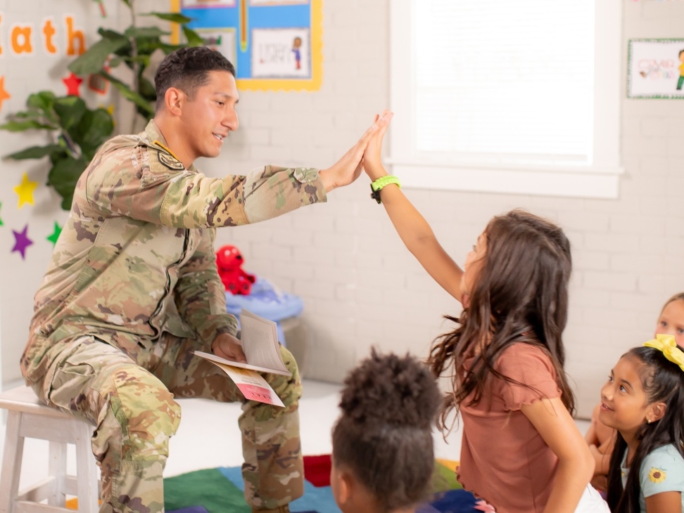 Soldier high-fiving a girl & engaging with students through reading.