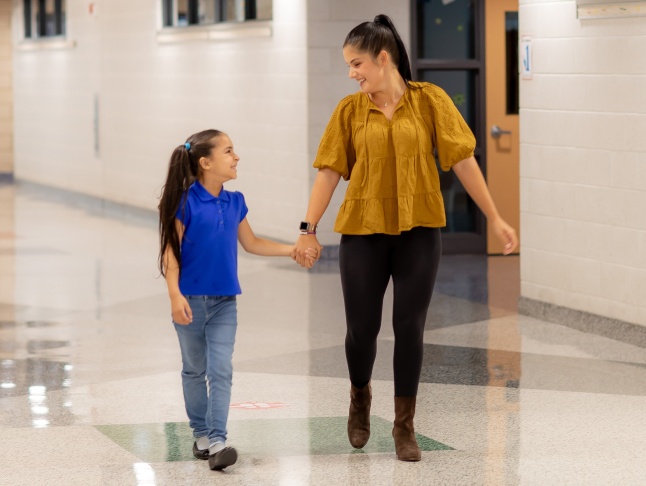 Parent holding a student's hand while walking down the hallway.